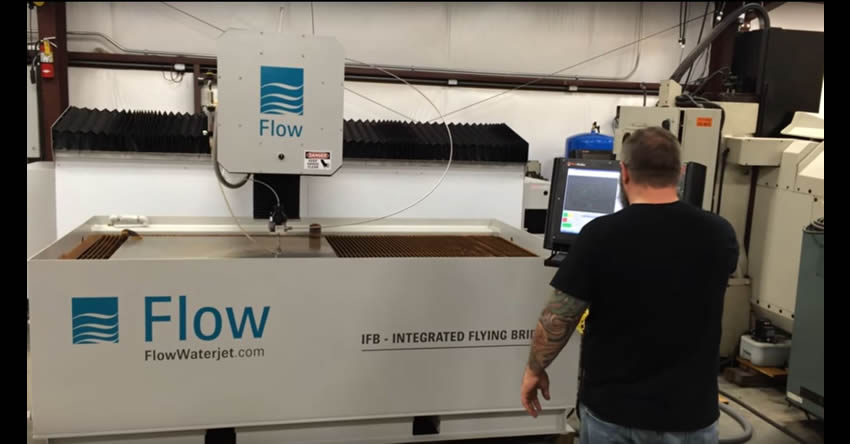 Man standing in front of large Flow CNC Waterjet, using a MachMotion CNC retrofitted control.